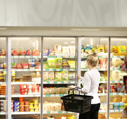 Woman choosing frozen food from a supermarket freezer, reading product information