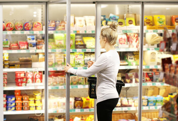 Woman choosing frozen food from a supermarket freezer, reading product information