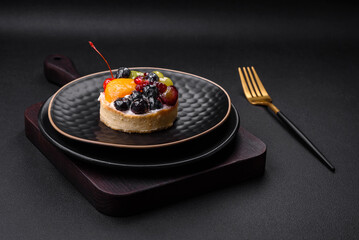 Delicious fresh tart with blueberries, cherries, grapes on a black ceramic plate