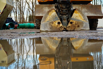 Excavator rusty bucket close-up and reflection in a puddle