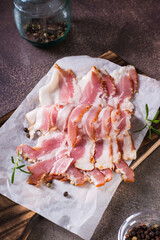 Raw bacon slices on paper on a cutting board on the table. Hearty snack. Vertical view