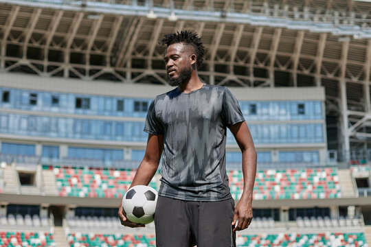 confident black football player holding the ball in his hand at the stadium