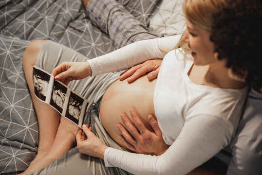 Pregnant Couple Looking At Ultrasound On A Bed