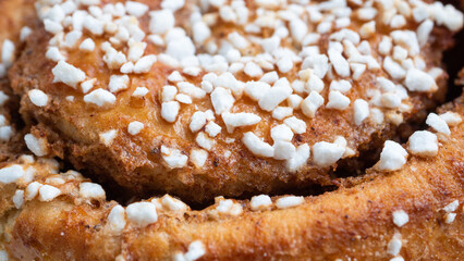 Highly detailed macro close up of a cinnamon bun. The sugar rocks are sticked to the buttery glazed bun, and the cinnamon spice make up the darker parts of this delicious Swedish pastry.
