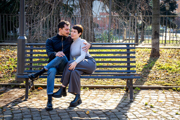 The young couple is sitting on a bench in the park in Rome. Beautiful couple in love is talking.