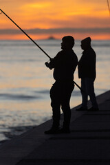 Two fishermen stand with fishing rods at sunset