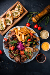 Plate beef and chicken barbecue with potato wedges, marinated red onion, fried mushrooms, garlic bread, sauces, tomatoes and greens.