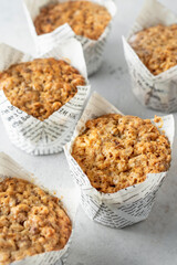 Oatmeal muffins in white paper cups on white textured background close up