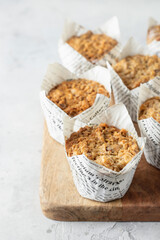 Oatmeal muffins in white paper cups on wooden board on textured background with copy space