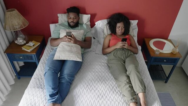 Married young black couple lying in the bed ignoring each other, typing or scrolling on smartphones. Young unhappy couple problem in bedroom. Divorce, marriage
