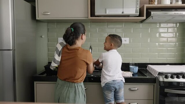 Son helping mom to clean the dishes, washing utensils together, household chores
