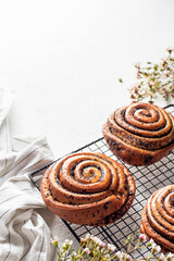 Sweet twisted buns with poppy seeds on cooling rack on white background with spring flowers, copy space