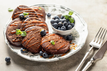 Healthy breakfast close up. Pancakes with fresh blueberries, syrup and mint leaves served with cutlery in morning light