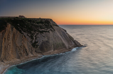 Colourful twilight with massive cliffs and sea on foreground, and the eighteenth century Sanctuary of Our Lady of Espichel Cape on background, Sesimbra, Setubal, Portugal