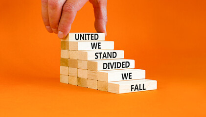United or divided symbol. Concept words United we stand divided we fall on wooden blocks. Beautiful orange table orange background. Businessman hand. Business united or divided concept. Copy space.