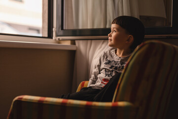 Little boy with fun hair cut looking out at windows while sitting on sofa.