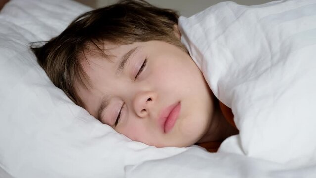 One happy boy sleeps in bed under blanket. The child at daytime relax. White linens. Dreaming time. Concept of soft and comfortable mattress and pillow. Soft pillow and warm blanket. The happy dreams.