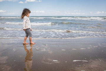 side view of little girl with brown hair walking along the sea coast on sand