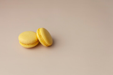 Two yellow macaroons on beige background close up copy space