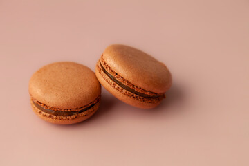 Two brown macaroons on brown-pink background close up copy space