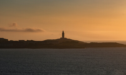Tower of Hercules on the horizon, illuminated by the last rays of sunlight at sunset. Located in A Coru&ntilde;a, Galicia, and of historical interest, copy space.