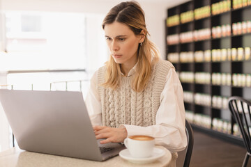 Thoughtful woman freelancer working on computer in cafe with coffee on table. Attractive...