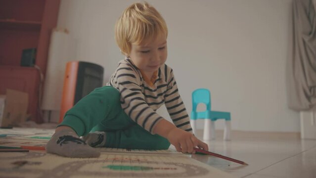 Cute little blonde boy playing with colored pencils on the floor