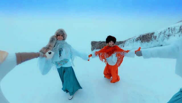 Girls in Russian folk costumes, shawls and long dresses spinning in a circle dance in winter on the street, Baikal, Siberia