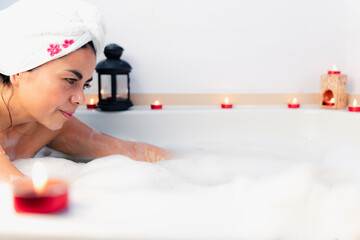 Latina woman taking bath with lots of foam and candles from spa of home.