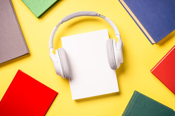 Audio books concept. Headphones and color books at yellow background. Flat lay image with copy...