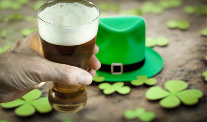 hand holding a beer, with a leprechaun's hat and 4-leaf clovers in the background