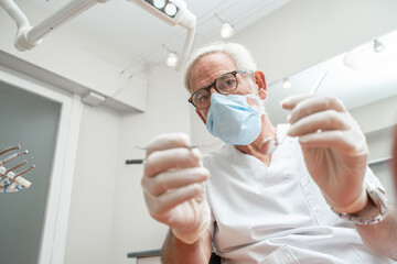 Close Up portrait of a mature experienced male doctor in glasses and face mask with dentist tools
