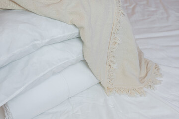 stack of white pillows and blankets lies on the bed on a white sheet on top, covered with a blanket