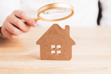Obraz na płótnie Canvas Hand holding magnifying glass and looking at house model, house selection, real estate concept.
