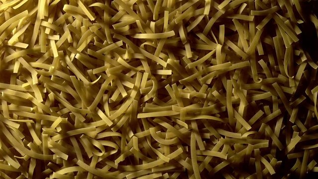 Uncooked Tagliatelle Lungo pasta - top view, flat lay, low key, food background. Light moves like the sunrise and sunset. Raw dried organic golden long macaroni texture. Italian food, cuisine and