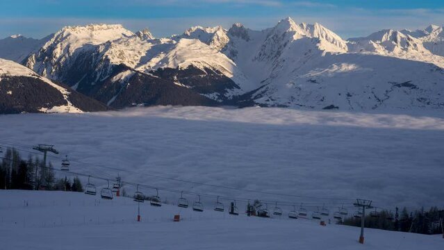Shade changes to sun lit ski slope in time lapse. Morning in ski resort La Plagne before opening of ski lifts. Moving inversion clouds in valley