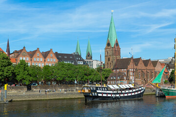 Naklejka premium Cityscape of Bremen with old architecture, historical wooden sailing ships and barge floating along the river Weser. Bremen, Germany, July 15, 2021
