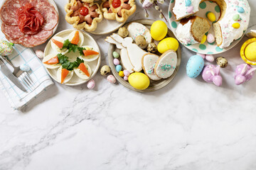 Festive dinner, Easter brunch. Easter table scene with an assortment of baking, desserts, stuffed eggs and dyed eggs on a marble background. View from above. Copy space.