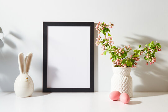 Mockup with a black frame and spring flowers in a vase, easter eggs on a light background. Empty poster frame mockup for presentation design, text, lettering