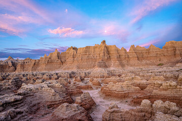 Pink sunrise clouds and full moon over rock formations in Badlands National Park