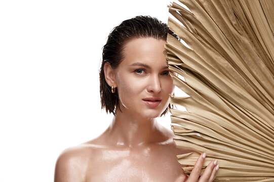 Middle aged naked caucasian woman with healthy wet skin and hair holds dry palm leave on white isolated background. Skin care beauty concept.
