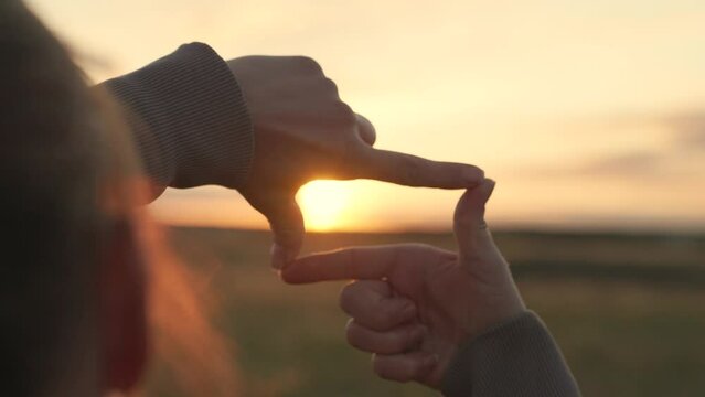 Business planning. Sees like in movies. Concept of seeing world as different. Hands of young female director cameraman making frame gesture at sunset in park.Girl shows her fingers frame symbol, sun