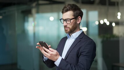 Handsome businessman in formal suit uses mobile phone in modern glass office Bearded male in glasses typing browsing chatting smartphone at workplace Indoor confident entrepreneur financier or broker - Powered by Adobe