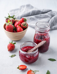 Strawberry jam in a jar on a light background with fresh berries. The concept of homemade delicious and healthy canned food