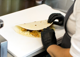 Chef with gloved hands in a fast food restaurant prepares a tortilla on the kitchen table