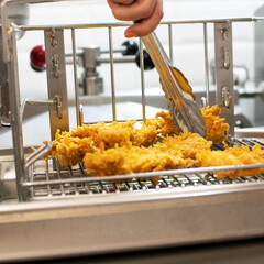 Hand of the cook with kitchen tongs takes a piece of cooked chicken in an appetizing crispy breading