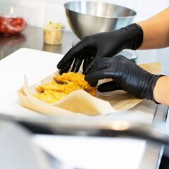 Hands of the chef in black gloves in the kitchen put pieces of appetizing fried breaded chicken into a cardboard package