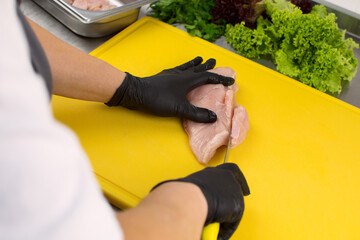 Hands of the cook in black gloves cut fresh chicken meat on a cutting board