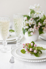 Beautiful table decor for a wedding dinner with a spring blooming apple tree flowers. Celebration of a special holiday marriage event. Fancy white plates, wineglasses