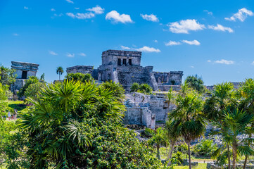 Fototapeta na wymiar A view past trees towards temple ruins at the Mayan settlement of Tulum, Mexico on a sunny day
